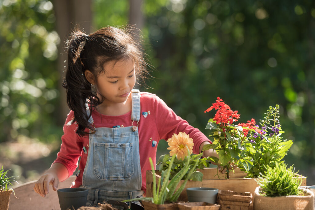 adorable asian little girl is planting spring flowers tree in pots in garden outside house, child education of nature. caring for new life. earth day holiday concept. world environment day. ecology.