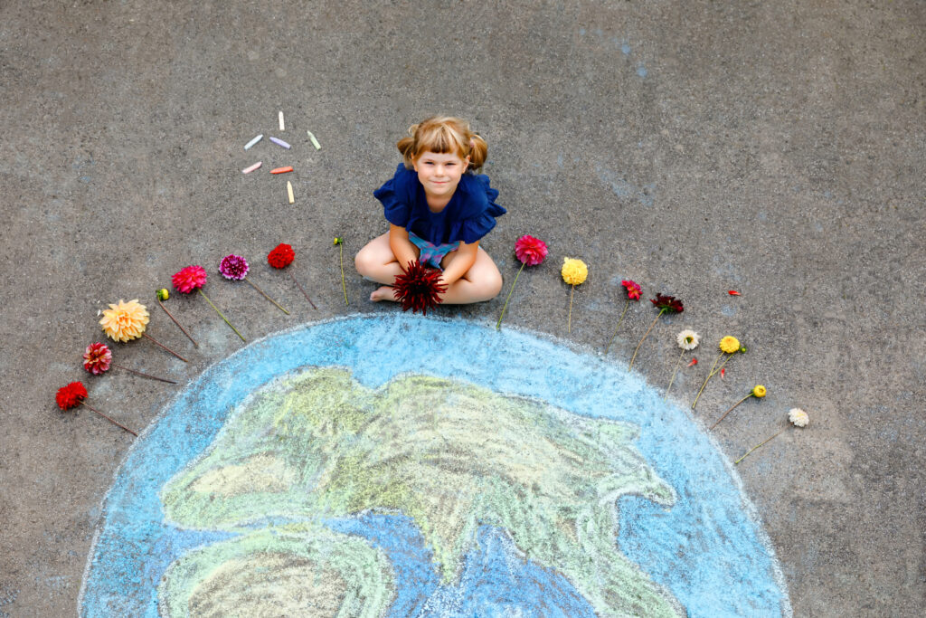 Little preschool girl with flowers and earth globe painting with colorful chalks on ground. Positive toddler child. Happy earth day concept. Creation of children for saving world, environment and ecology